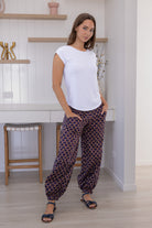 Woman wears cotton floral print harem pants with a wide waistband, with hands in pockets