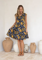 Woman wearing retro inspired cotton knee length dress in yellow, green and grey florals on black base.