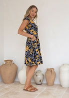 Model posing sideways in a beautiful cotton dress with yellow, pear green and grey florals on the black base.