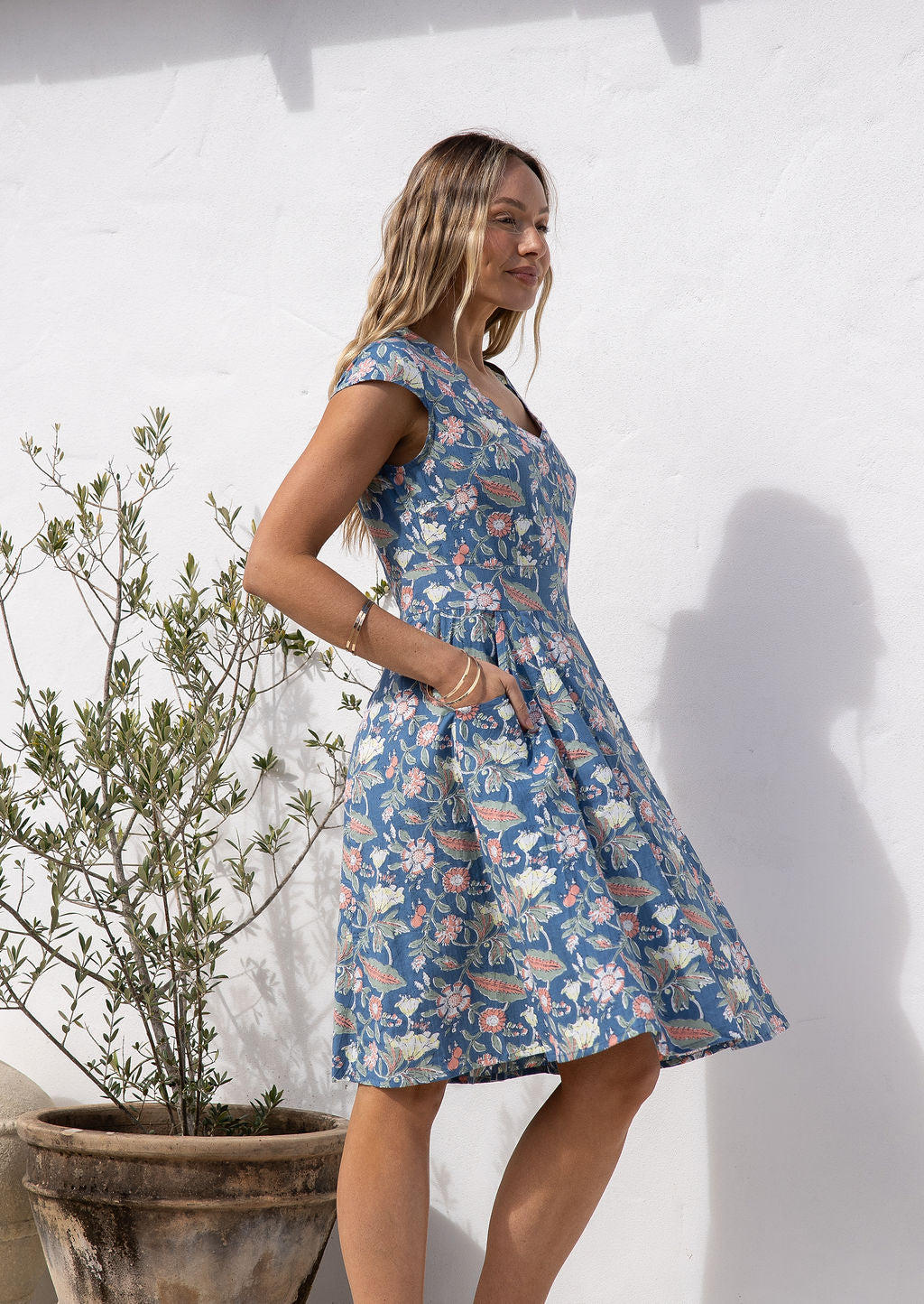 Model stands side ways in retro style 100% cotton blue floral with cross over bodice and pockets, fit and flare style 