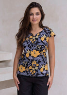 A woman poses in a cap-sleeved cotton tailored top with a retro floral print in yellow, grey, and green on a black base