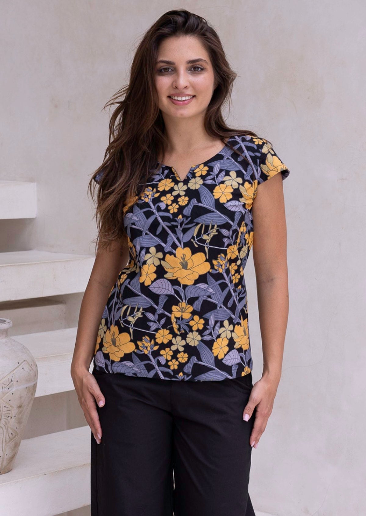 A woman wears a 100% cotton tailored top with short cap sleeves and a round neckline with a keyhole cutout, paired with black cotton pants
