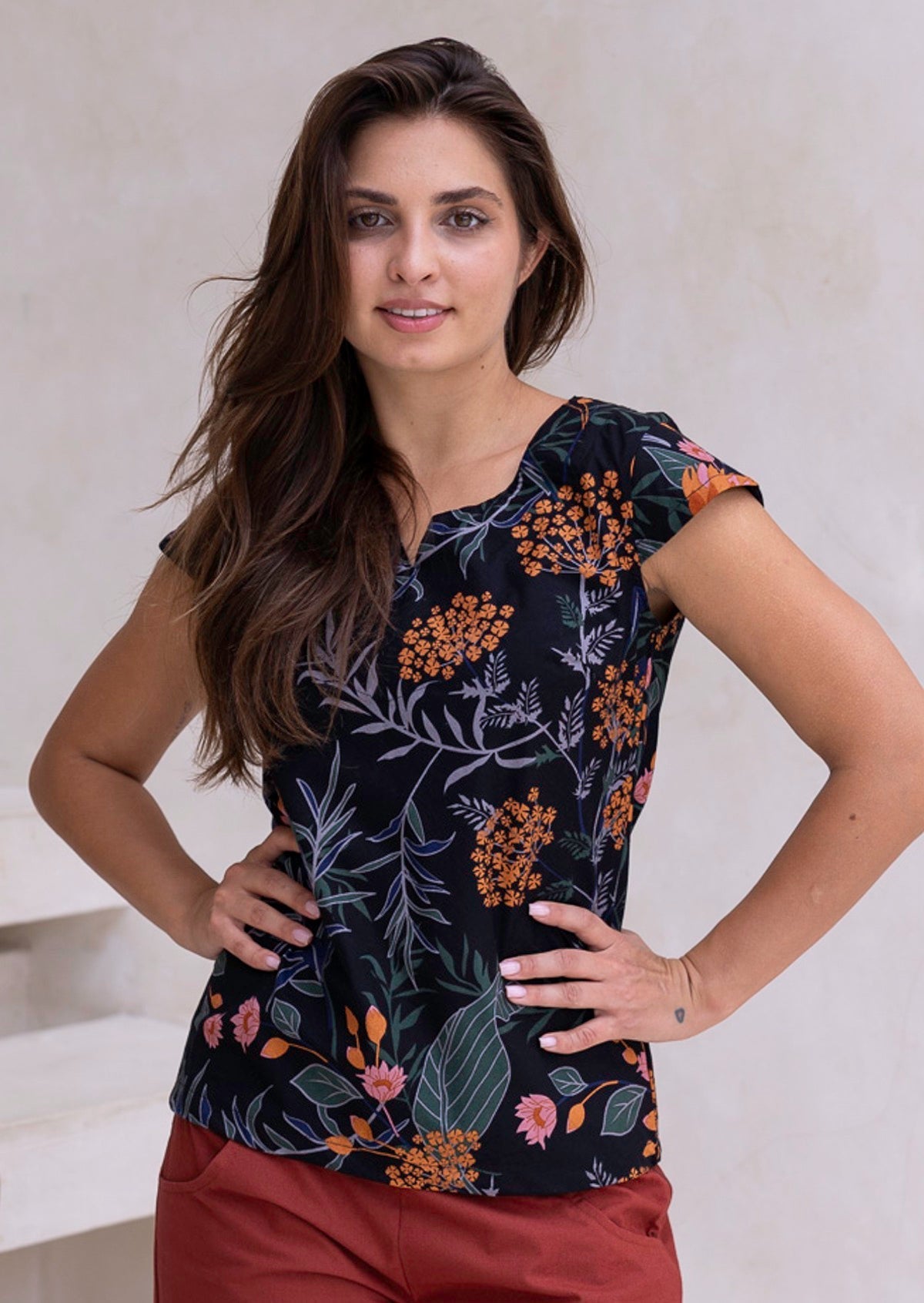 Woman poses in cap sleeved cotton tailored top in black based botanical print with orange and pink florals.