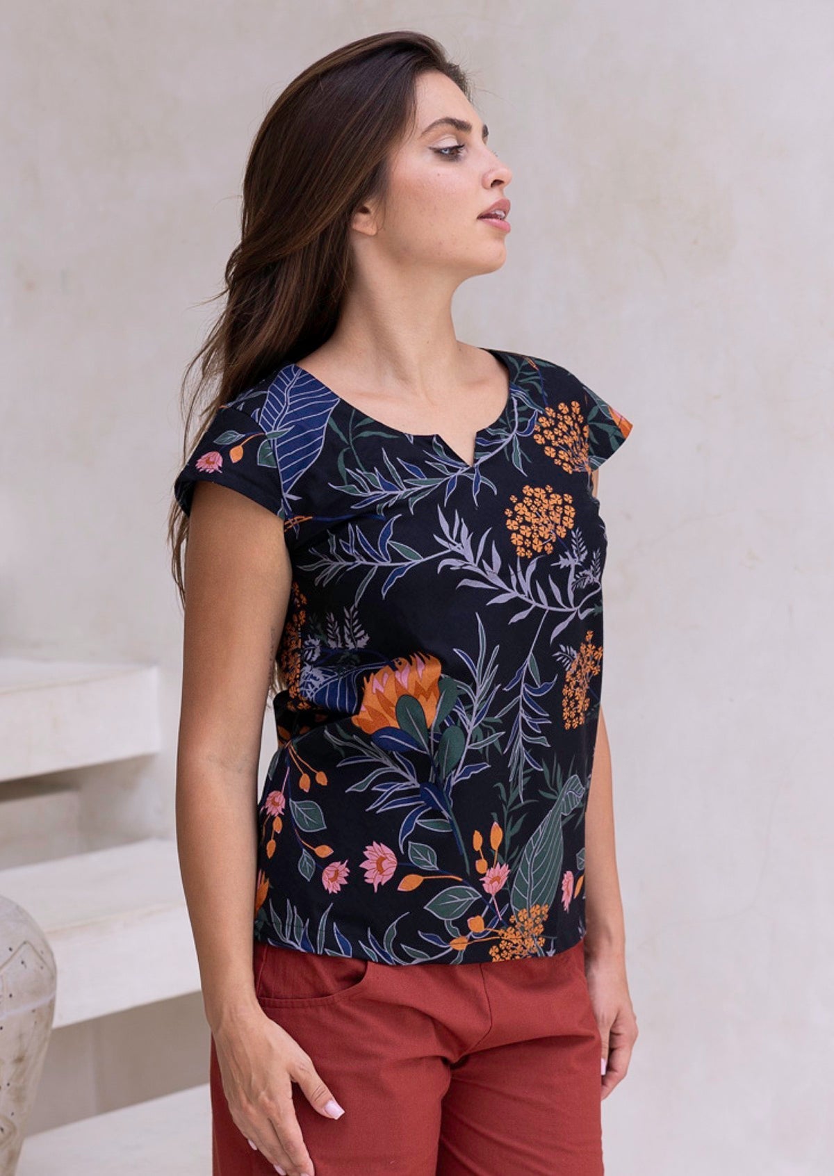 Woman wearing cap sleeved black based botanical print top with orange, pink florals and blue, grey and green leafy print.
