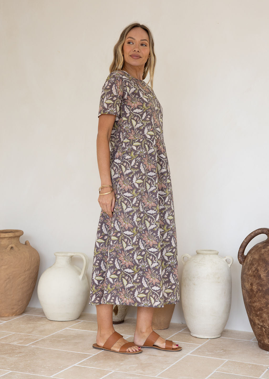 Model stands in relaxed fit cotton sundress with high round neckline, short sleeves and white, beige, coral pink and lime florals over taupe background.