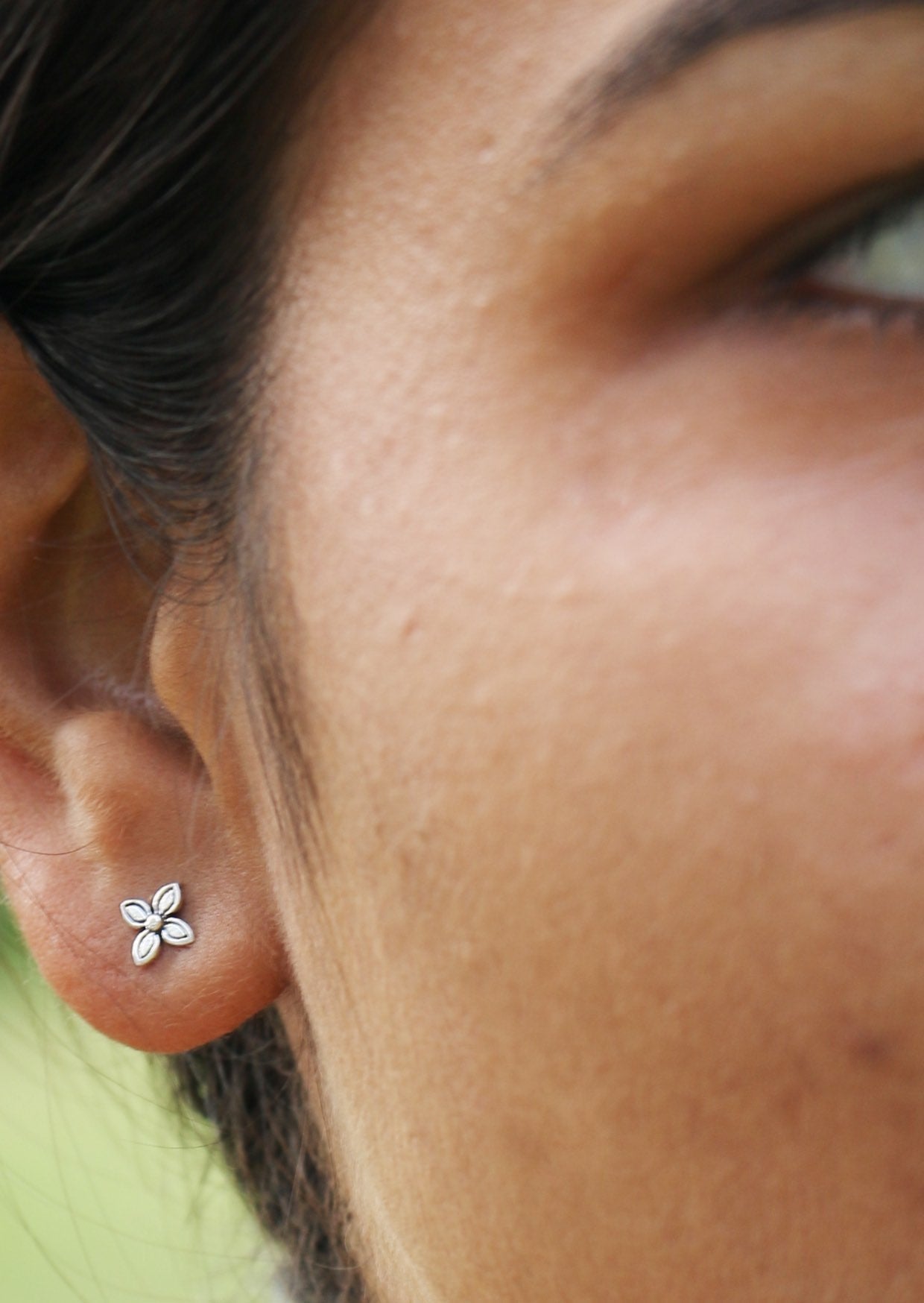 Woman is wearing sterling silver Baronia studs with four smooth, curved petals 