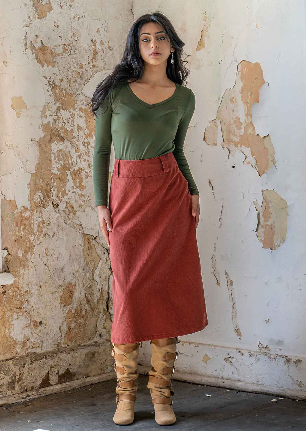 Model poses in midi length corduroy A-line skirt in burnt henna colour, paired with an olive long sleeve rayon top and boots