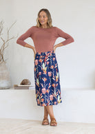 Woman wearing a cotton midi length A-line skirt with belt loops in native pink and green floral print.