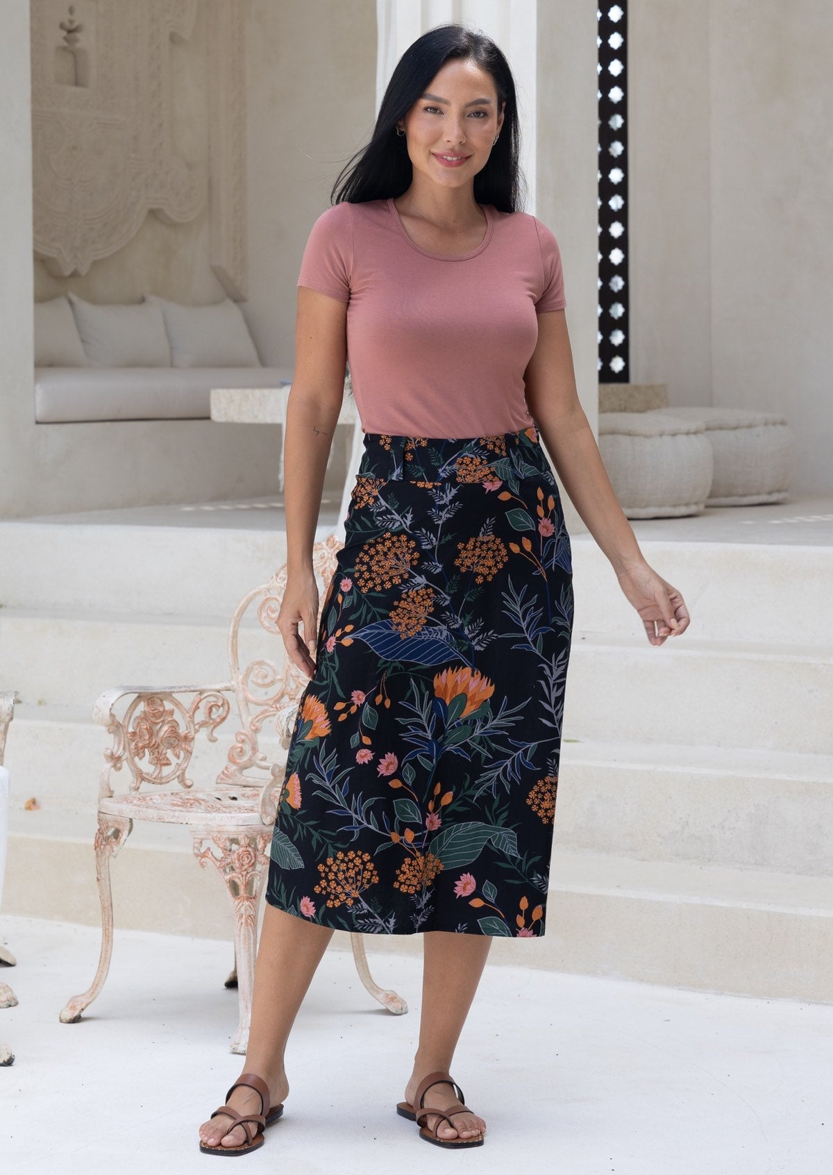 Woman wearing a pink top and a black based cotton floral midi length skirt