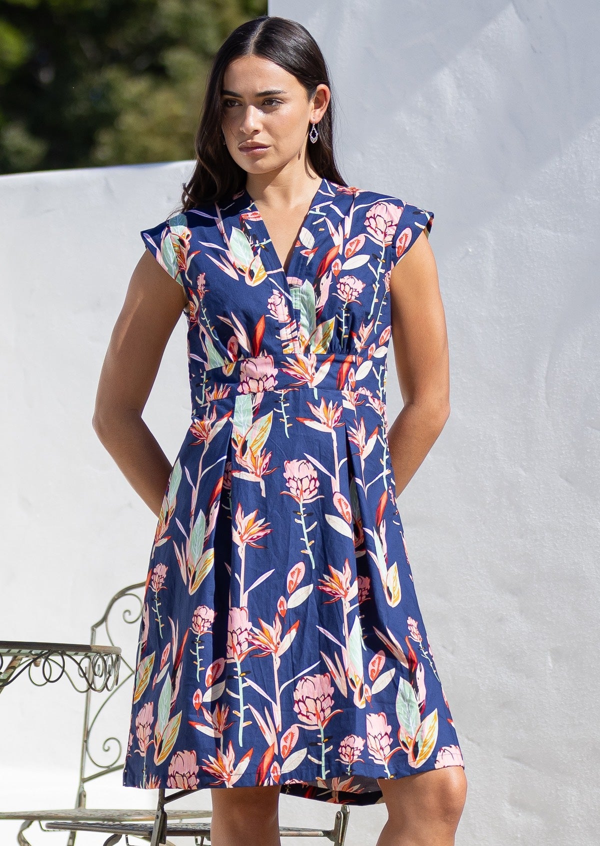 Woman wears  above knee length cotton dress with V neckline, cap sleeves and softly cinched waist.