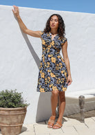 Model wearing a knee length black floral cotton dress with cinched waist, box pleats and cap sleeves 