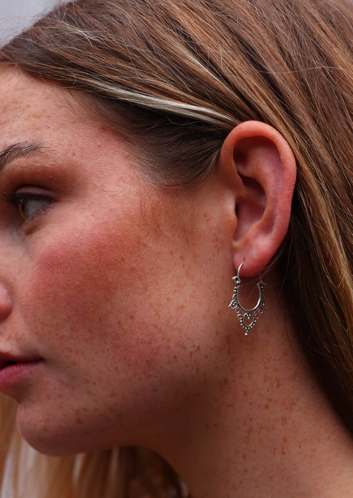 Woman wears sterling silver wire hook earrings with spiral and bead details