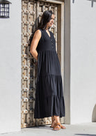 Woman wearing a black maxi dress standing in front of a textured wooden door.