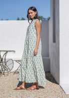 Woman wearing a long white floral cotton dress standing outdoors near a white wall.