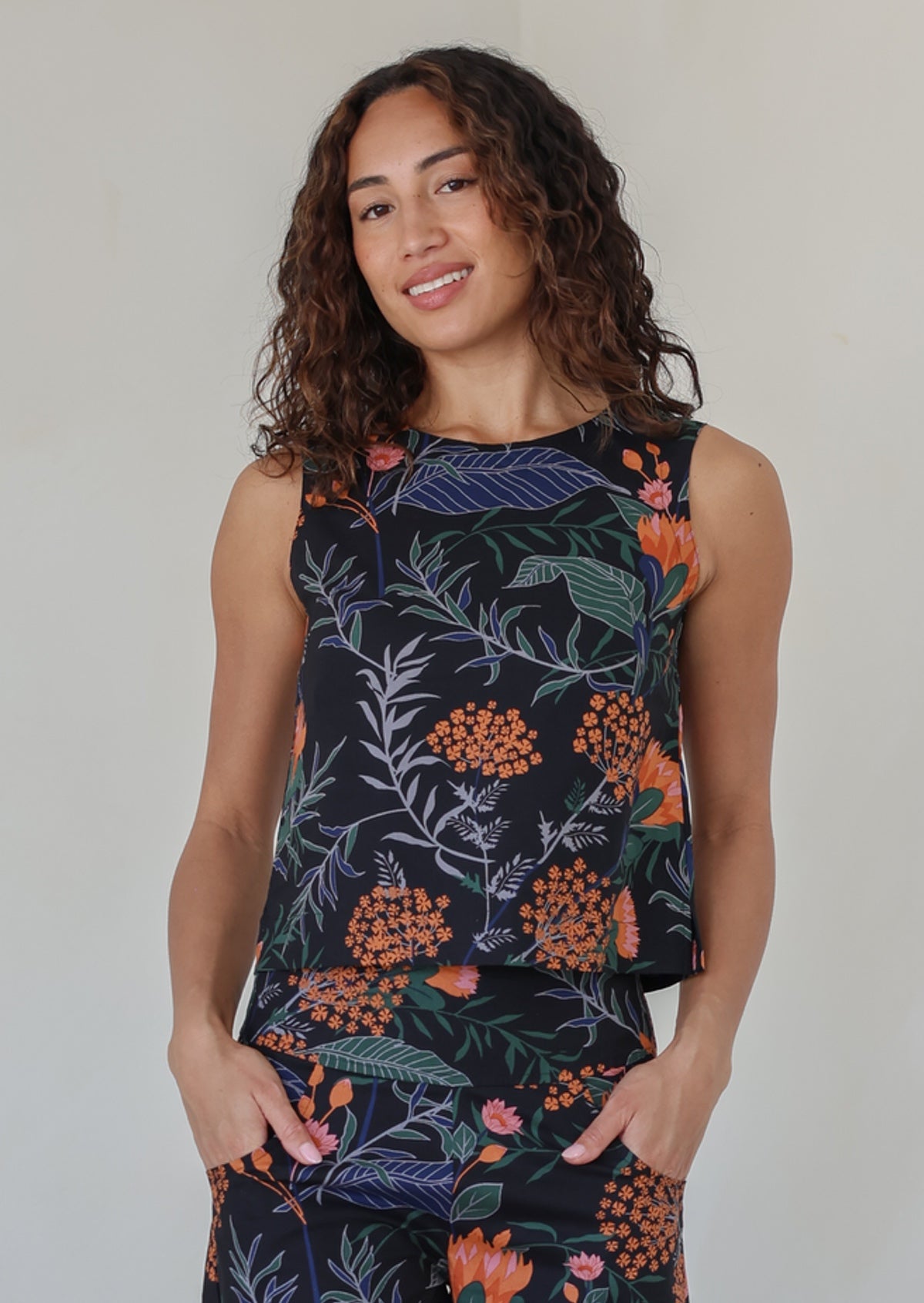 Woman wearing a sleeveless cotton top featuring high round neckline in gorgeous black based botanical print with pink and orange florals