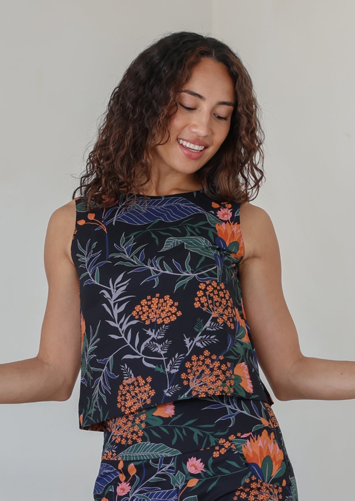 Woman wearing a relaxed fit sleeveless floral top against a plain background