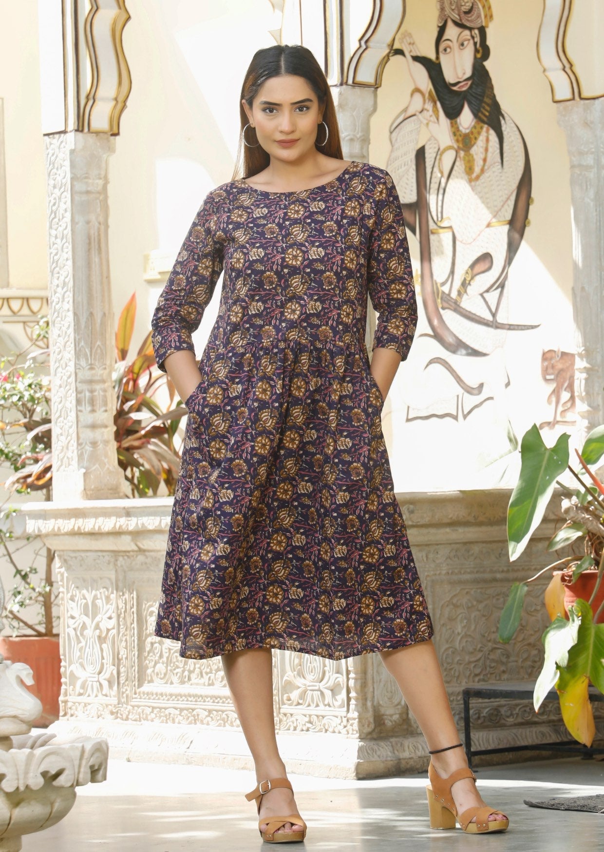 Model with dark hair wears 100% cotton relaxed fit dress in purple based pink ,cream and light brown floral print.