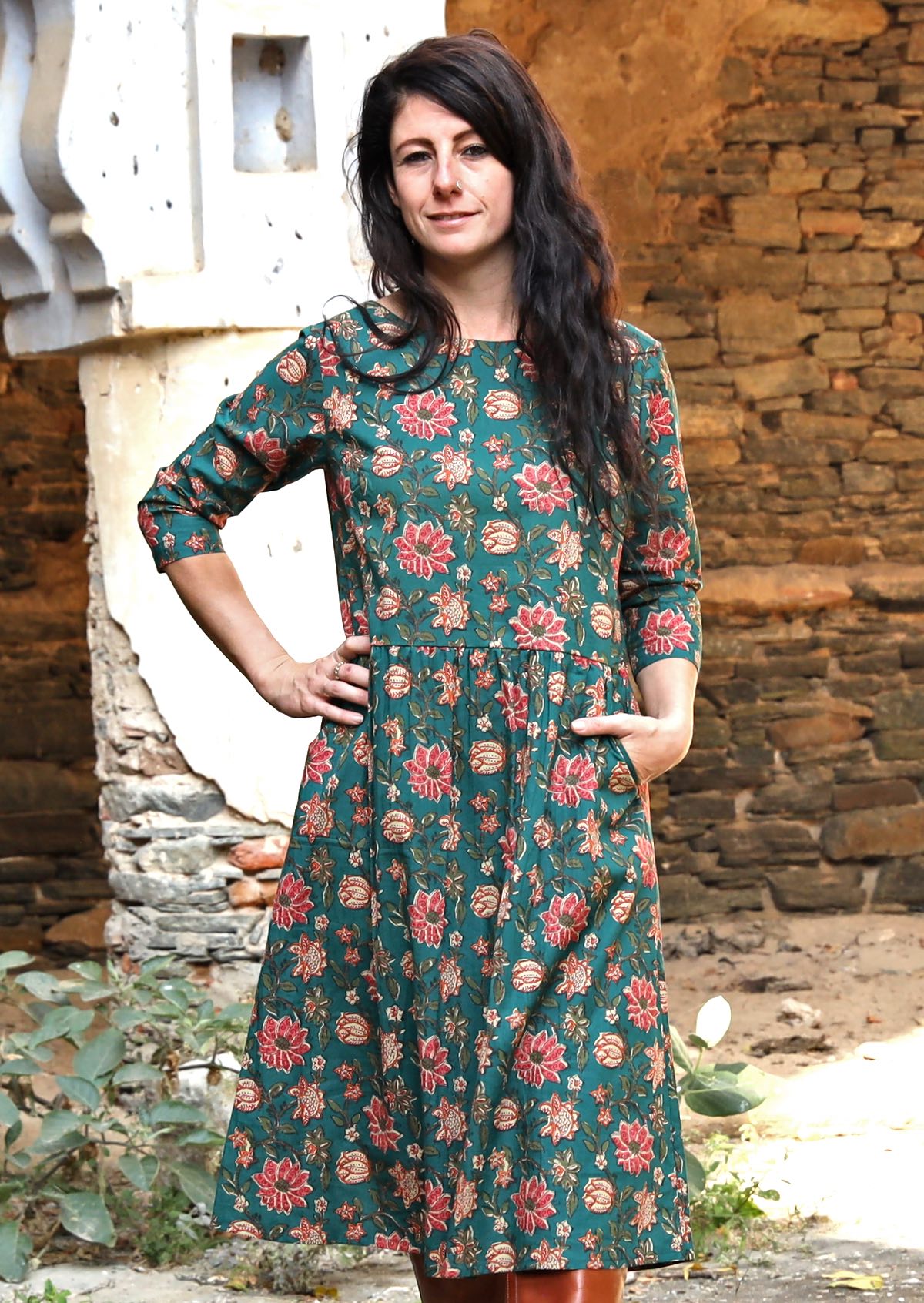 Model in black hair embracing a 100% cotton dress with boat neckline, 3/4 sleeves and one hand in pocket.
