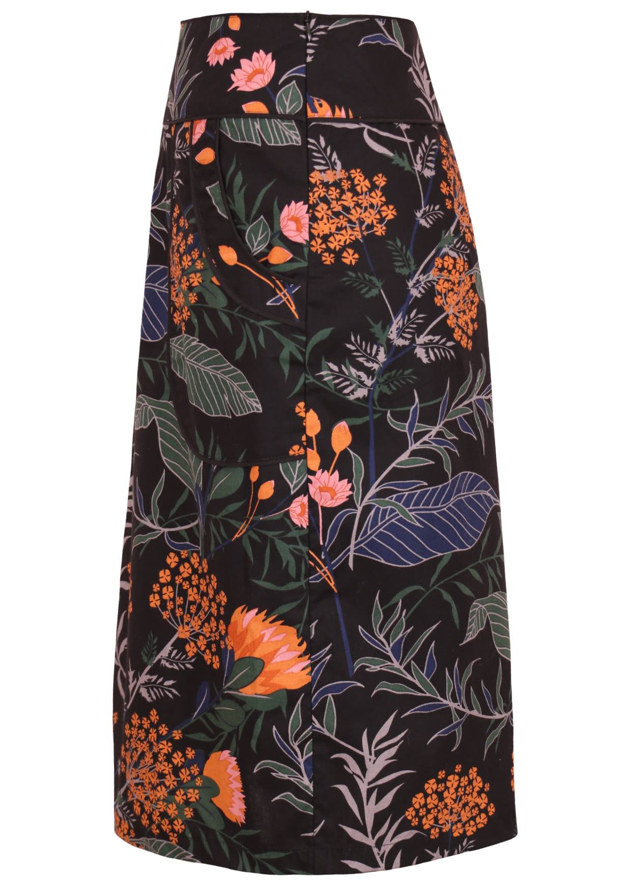Side view of knee-length cotton pencil skirt with side zipper and piped details in retro floral print with orange, pink, blue, and green on black base