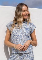 Woman wearing a white based blue floral print cotton shirt in a natural setting.