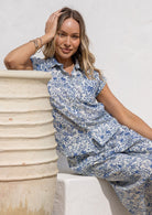 Woman wearing a white based blue floral print button up cotton shirt.