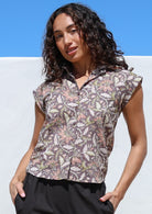 Woman wearing a taupe based floral printed slim fit shirt, against a blue and white background