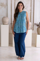 Woman wearing a blue 100% cotton patterned top and dark blue cotton pants in a decorative setting.