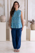 Woman wearing a summer cotton blouse in aqua blue navy pants standing in a decorative room with white walls and vases.