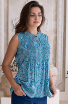 Woman wearing a aqua blue patterned sleeveless cotton blouse and dark blue cotton pants standing in a decorative room.