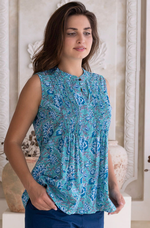 Woman wearing a aqua blue patterned sleeveless cotton blouse and dark blue cotton pants standing in a decorative room.