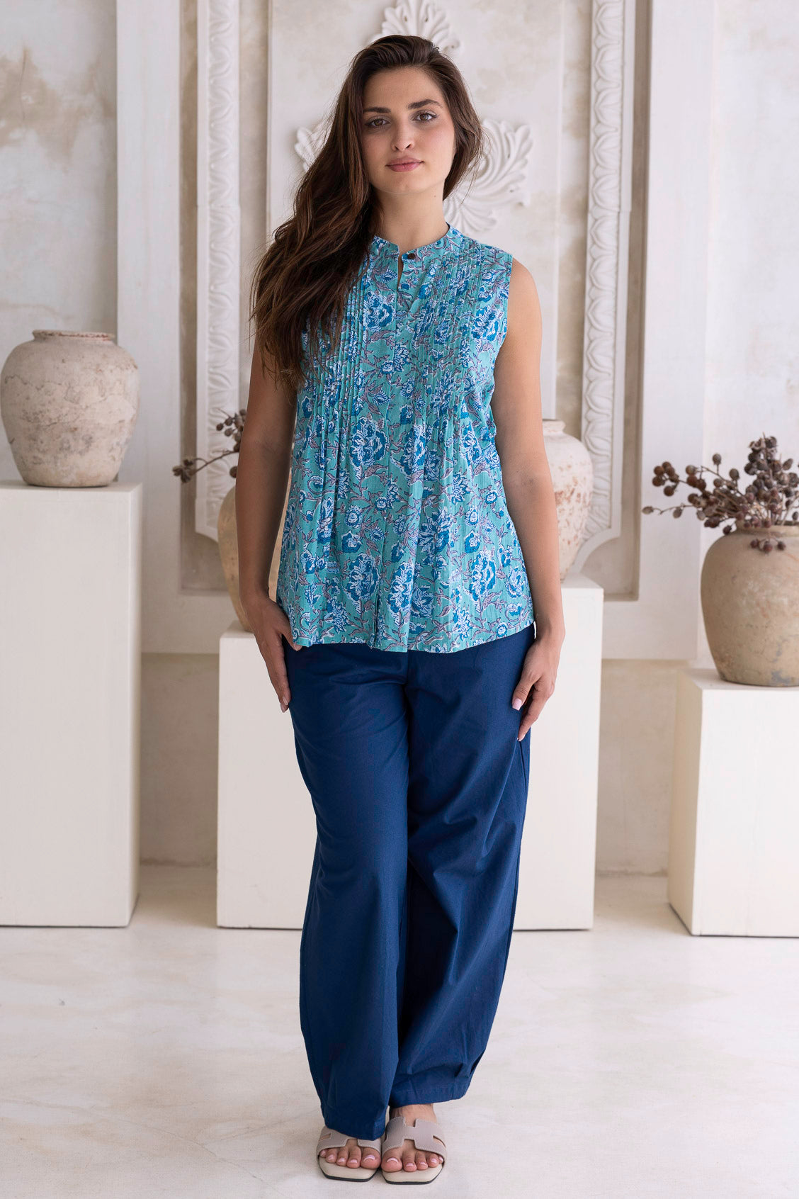 Woman wearing a blue cotton floral top and navy pants standing in a room with decorative elements.
