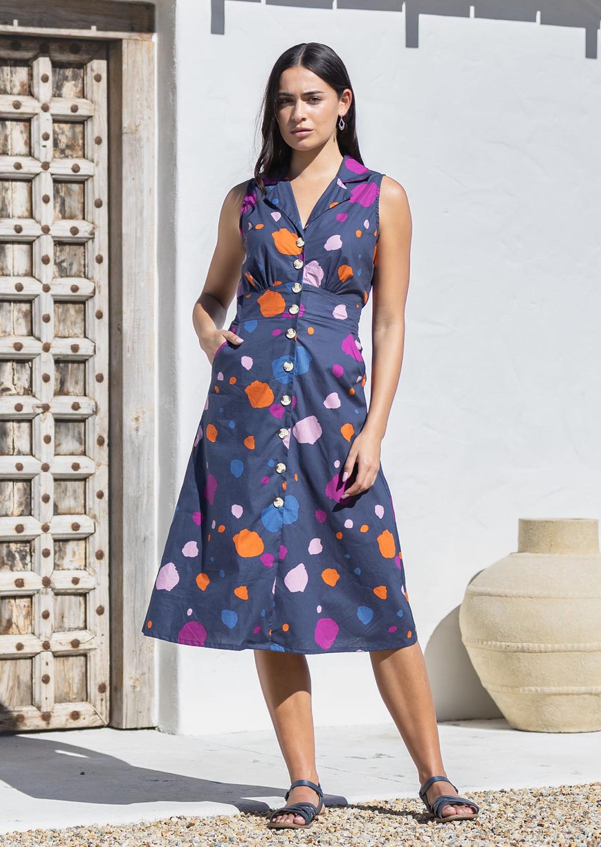 Woman wearing sleeveless, button through cotton dress with collar and pockets.