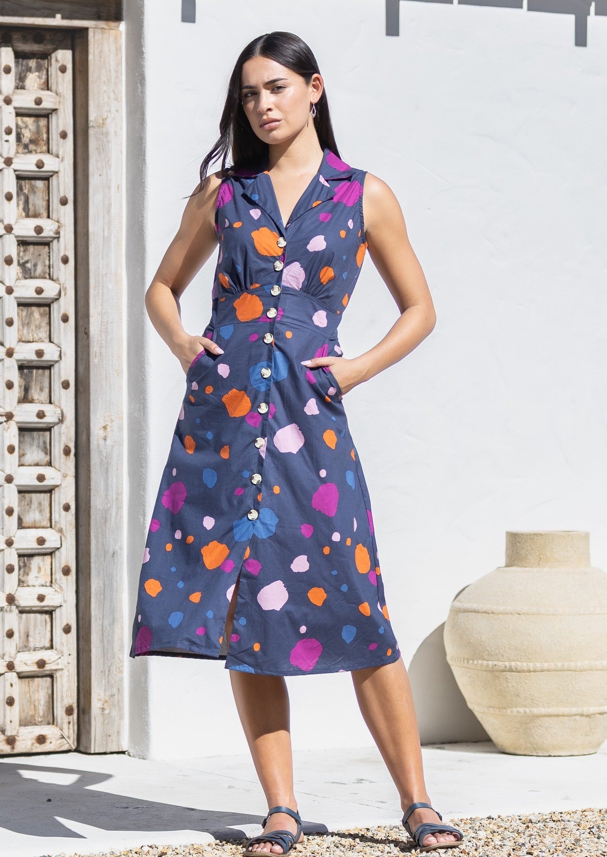 Woman with hands in pocket wears 100% cotton midlength dress in colorful spotty print on navy base.