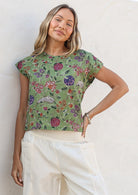 Woman wearing a moss green floral cap sleeve cotton top against a white wall