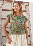 Woman wearing a moss green floral cotton top against a wooden door.