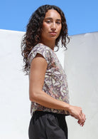 Model wearing a simple lightweight cotton top with delicate florals in pink, lime, and beige on a taupe base