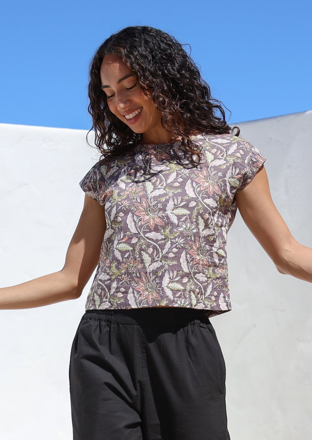 Model wears lightweight 100% cotton top with cap sleeves and high round neckline in taupe based delicate floral print