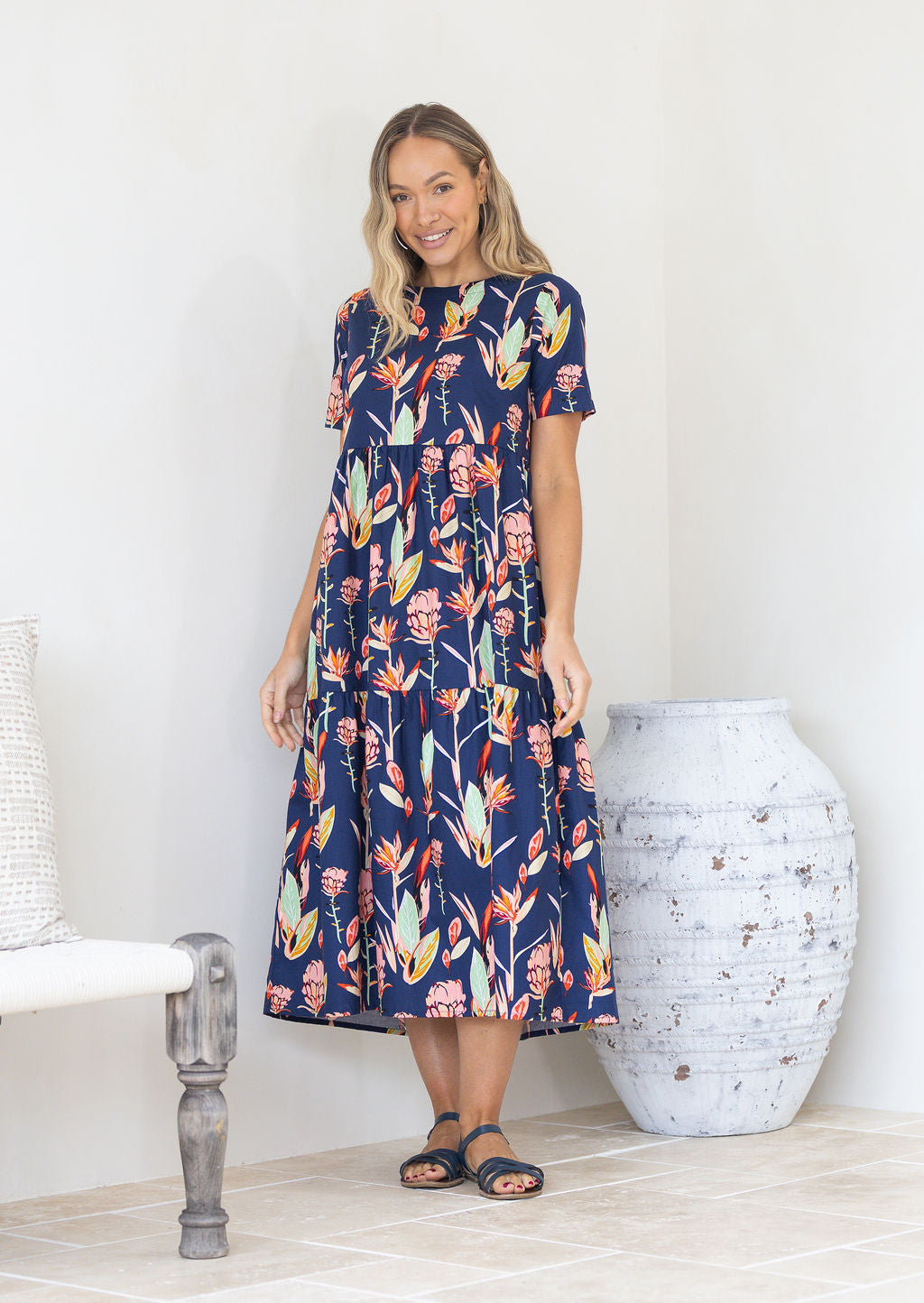 Woman standing near a decorative vase wears 100% cotton mid length dress with pockets.
