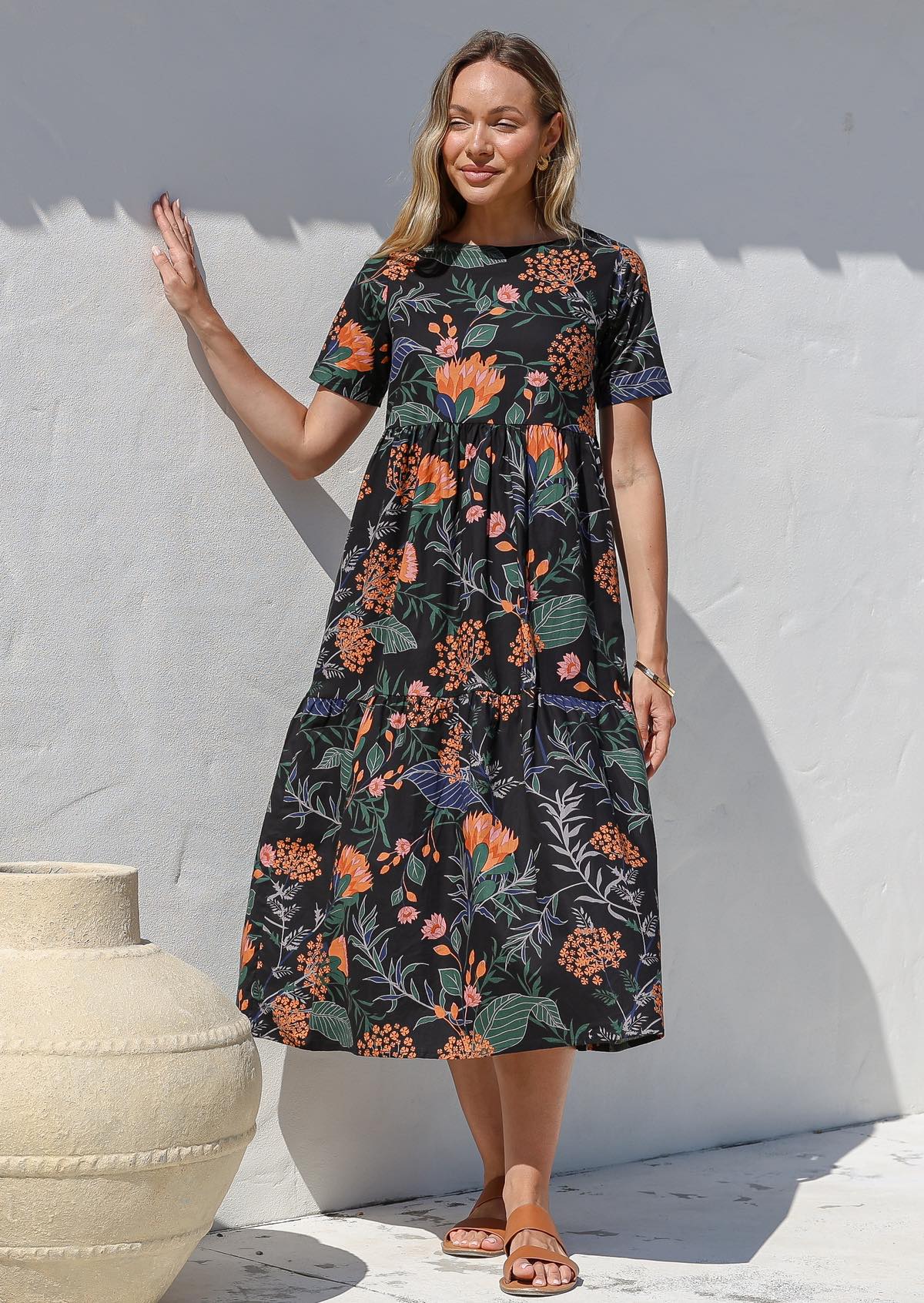 Woman wearing a black based floral cotton midi length dress with tiered skirt and short sleeves