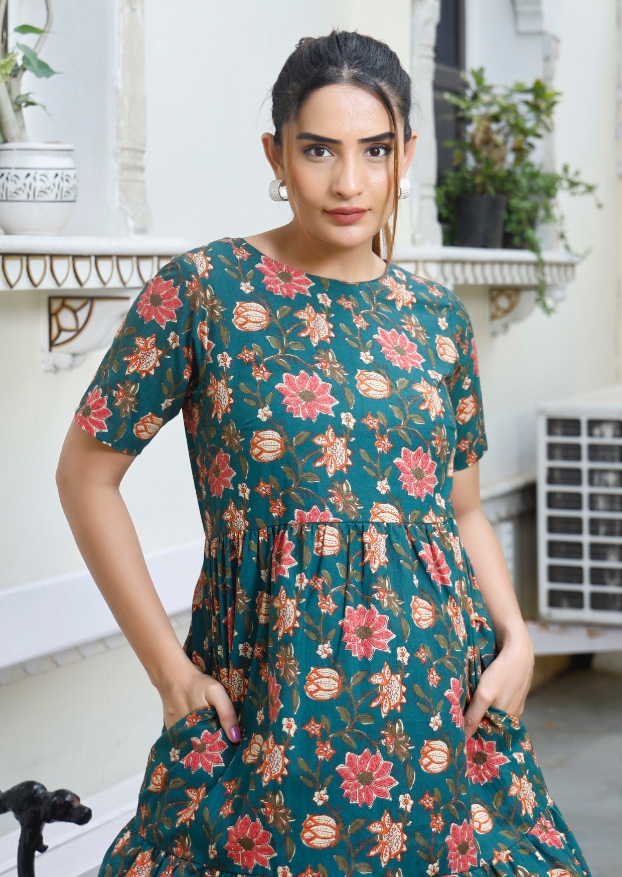 Model in green floral print dress with round neckline, short sleeves and hands in pocket 
