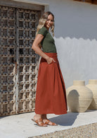 Woman wearing basic olive green top paired with cotton button through a-line skirt with box pleats and pockets in burnt henna shade