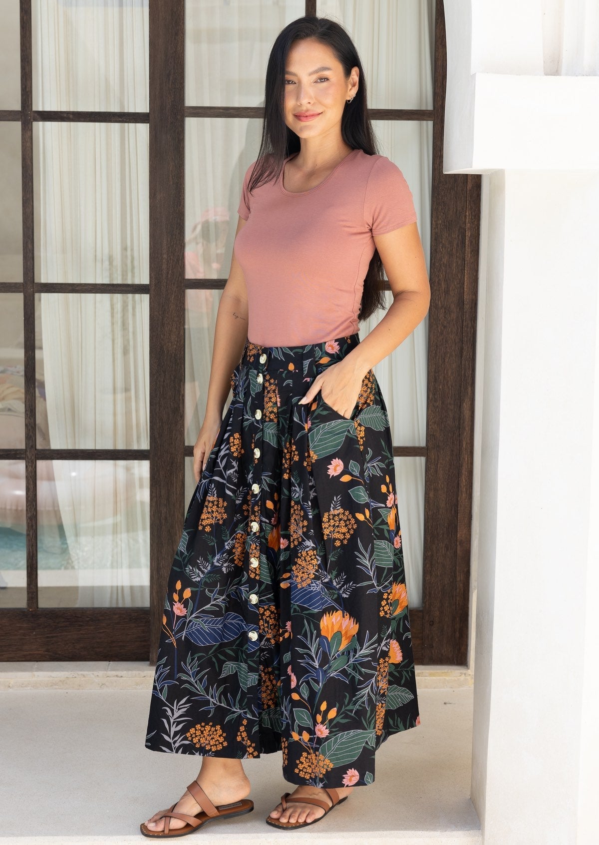 Woman standing in a button throgh midi length skirtin a black based floral print, with her hand in pocket