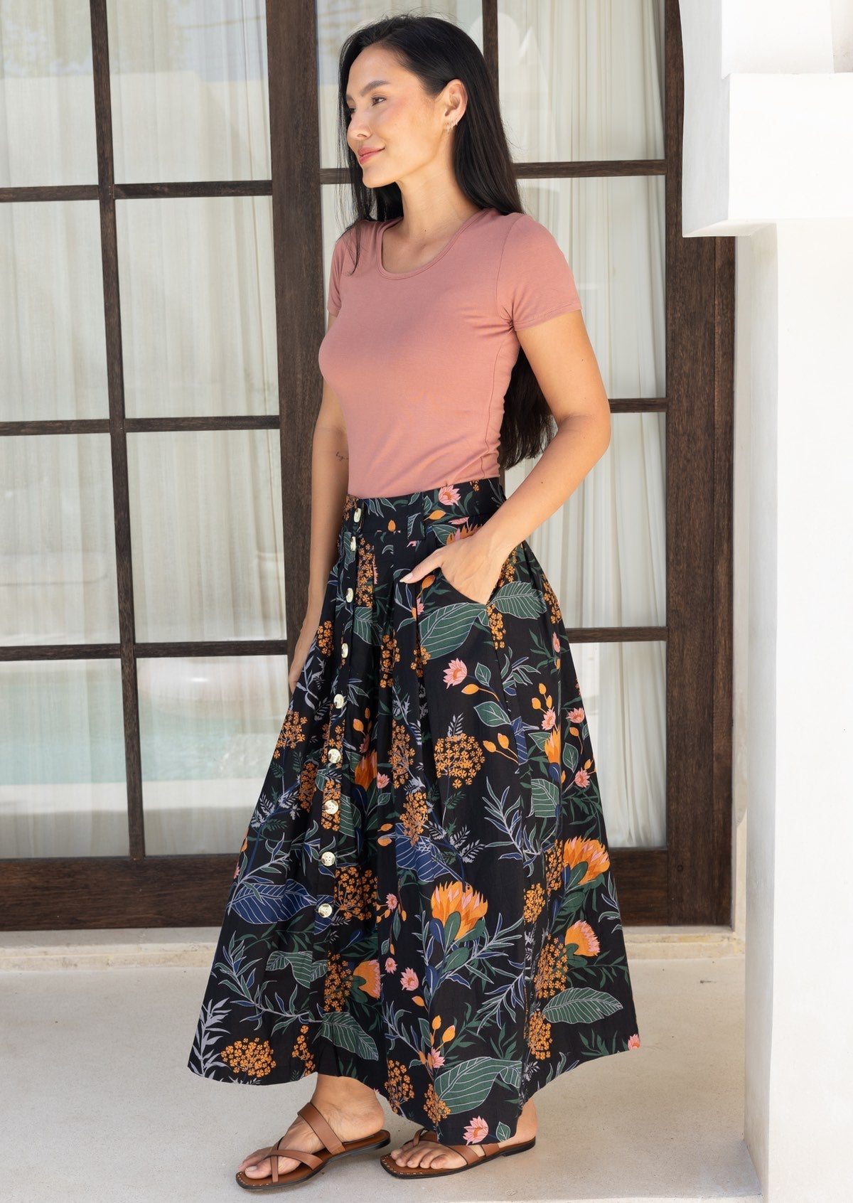 Woman wearing a dusty pink top and black based cotton floral midi length skirt