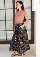 Woman wearing a dusty pink top and black based cotton floral midi length skirt
