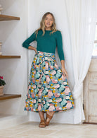 Woman wearing a teal top and pastel print shin length skirt with box pleats and belt loops