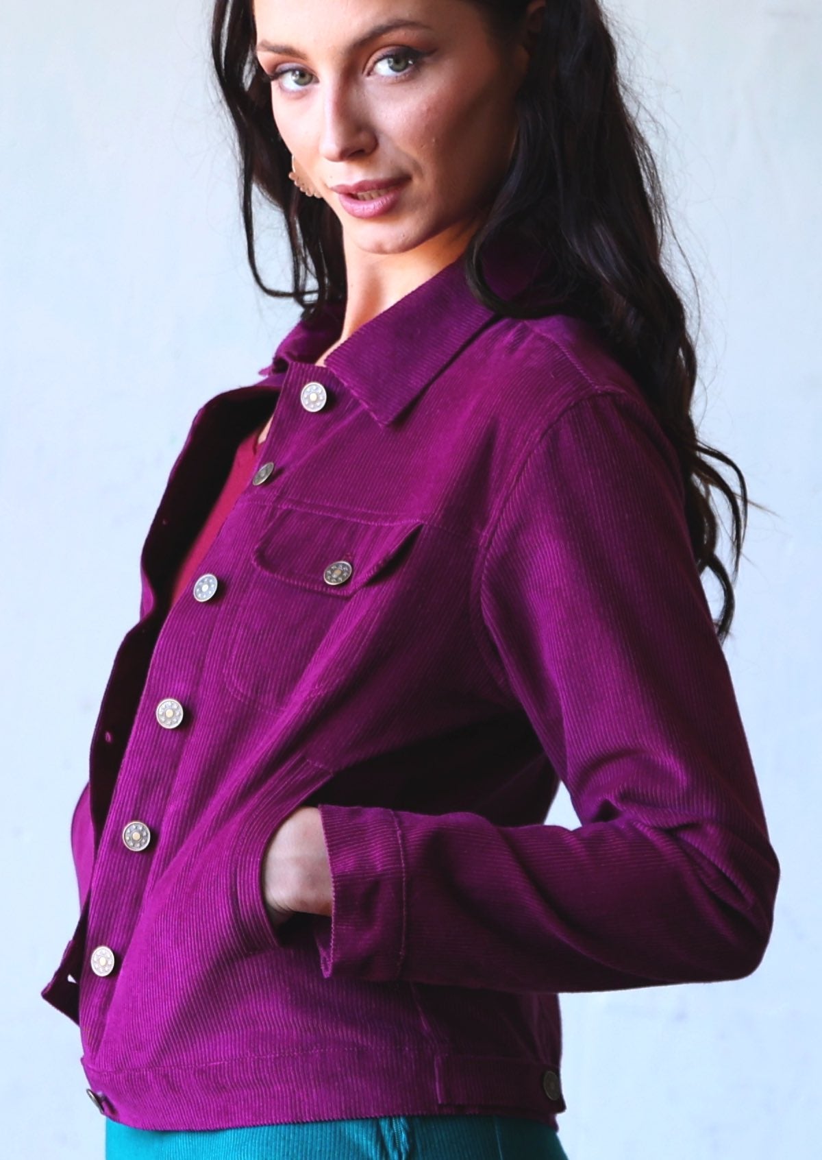 Woman wearing collared purple 100% cotton corduroy jacket with brass buttons, and breast and front pockets