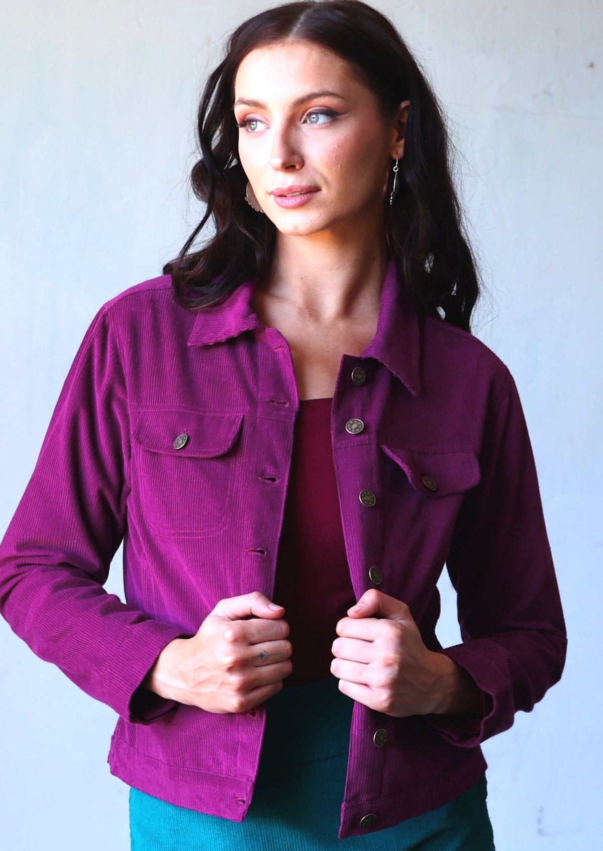 Woman wearing purple corduroy jacket with breast and front pockets, and brass buttons