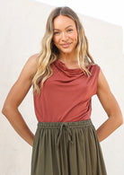 Woman wearing a terracotta coloured sleeveless top with a cowl neckline, tucked into olive green skirt