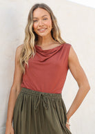 Woman wearing a terracotta coloured sleeveless top and olive green skirt against a white background