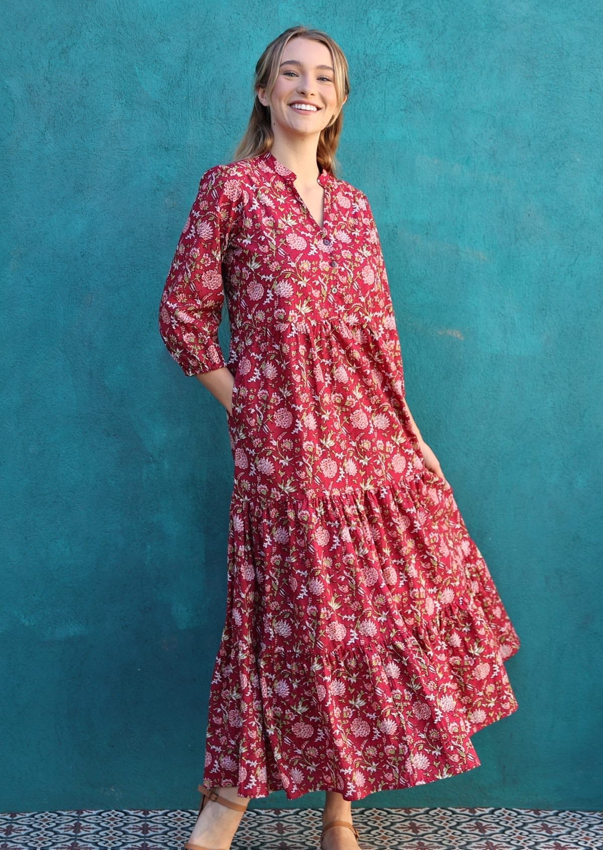Woman wears cotton tiered maxi dress with a buttoned bodice with a V-neckline and mandarin collar, and 3/4 sleeves, with hand in pocket